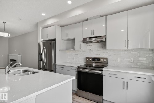 Kitchen featuring gloss white cabinetry, white countertops, stainless steel appliances, and a tiled backsplash - 4879 Alwood Point(E) Sw, Edmonton, AB - Indoor Photo Showing Kitchen With Double Sink With Upgraded Kitchen