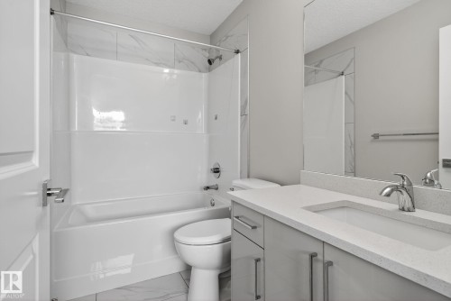 Bathroom featuring a white tub and shower combination with a tiled surround, a toilet, a vanity with a white countertop and integrated sink, and a large wall-mounted mirror - 4879 Alwood Point(E) Sw, Edmonton, AB - Indoor Photo Showing Bathroom