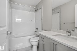 Bathroom featuring a white tub and shower combination with a tiled surround, a toilet, a vanity with a white countertop and integrated sink, and a large wall-mounted mirror - 