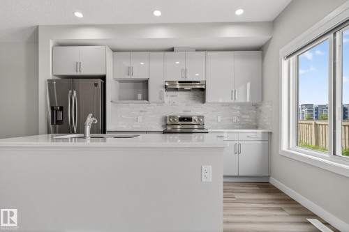 Modern kitchen featuring light gray cabinetry, stainless steel appliances, a tile backsplash, light-toned countertops, and wood-finish flooring - 4879 Alwood Point(E) Sw, Edmonton, AB - Indoor Photo Showing Kitchen With Upgraded Kitchen