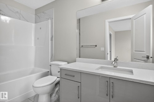 Contemporary bathroom featuring a white bathtub/shower combination, marble-look tile surround, light gray vanity with integrated sink, and a large wall-mounted mirror - 4879 Alwood Point(E) Sw, Edmonton, AB - Indoor Photo Showing Bathroom