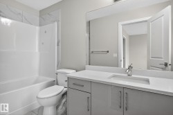 Contemporary bathroom featuring a white bathtub/shower combination, marble-look tile surround, light gray vanity with integrated sink, and a large wall-mounted mirror - 