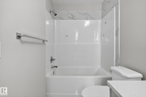 Bathtub with a shower, tile surround, polished chrome fixtures, and a white toilet - 4879 Alwood Point(E) Sw, Edmonton, AB - Indoor Photo Showing Bathroom