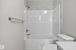 Bathtub with a shower, tile surround, polished chrome fixtures, and a white toilet - 