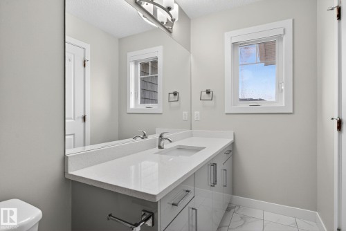 Contemporary vanity with an integrated sink, polished chrome faucet, and expansive wall-mounted mirror - 4879 Alwood Point(E) Sw, Edmonton, AB - Indoor Photo Showing Bathroom