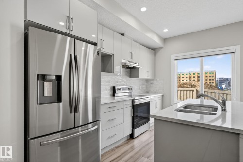 Full-size stainless steel refrigerator, white shaker cabinetry, light-toned wood-finish flooring, undermount double-basin sink, and a large window - 4879 Alwood Point(E) Sw, Edmonton, AB - Indoor Photo Showing Kitchen With Double Sink With Upgraded Kitchen