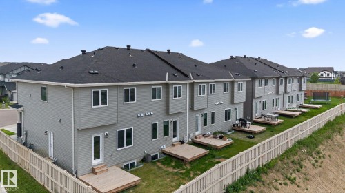 Rear exterior showcasing multiple units with gray siding, individual wooden decks, and a shared grassy area enclosed by a light wood fence - 4879 Alwood Point(E) Sw, Edmonton, AB - Outdoor