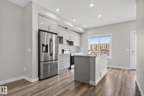 Kitchen featuring wood-finish flooring, stainless steel appliances, light gray cabinetry, and a center island with an undermount sink - 4879 Alwood Point(E) Sw, Edmonton, AB - Indoor Photo Showing Kitchen With Upgraded Kitchen