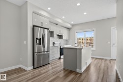 Kitchen featuring wood-finish flooring, stainless steel appliances, light gray cabinetry, and a center island with an undermount sink - 