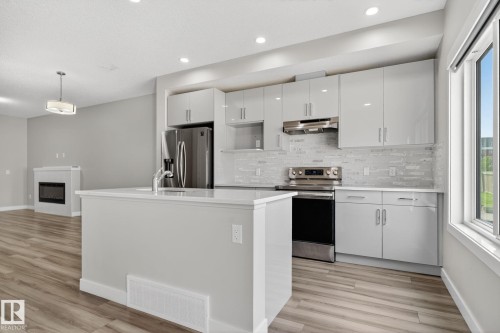 Kitchen with wood-finish flooring, white cabinetry, a white countertop island, stainless steel appliances, and a tiled backsplash - 4879 Alwood Point(E) Sw, Edmonton, AB - Indoor Photo Showing Kitchen With Upgraded Kitchen