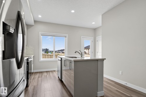 Kitchen featuring an island with an integrated sink, wood-finish flooring, recessed lighting, and a window - 4879 Alwood Point(E) Sw, Edmonton, AB - Indoor Photo Showing Kitchen