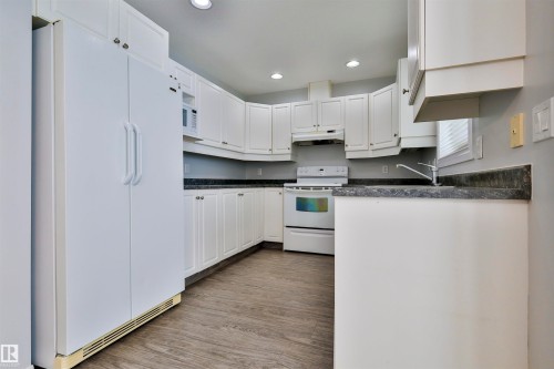 Kitchen featuring extensive white cabinetry, dark countertops, white appliance package, recessed lighting, and wood-finish flooring - 15529 95 Avenue Nw, Edmonton, AB - Indoor Photo Showing Kitchen
