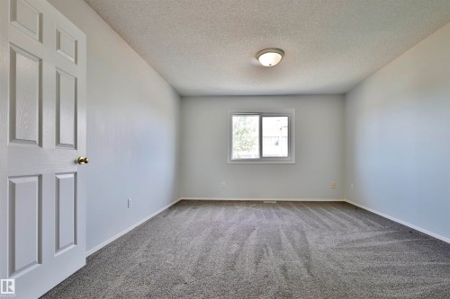 Neutral wall color, wall-to-wall carpeting, overhead lighting, window with a window sill, and a paneled door with a brass knob - 15529 95 Avenue Nw, Edmonton, AB - Indoor Photo Showing Other Room
