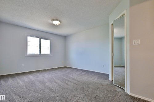 Spacious room featuring neutral carpeting, a large window, and mirrored sliding closet doors - 15529 95 Avenue Nw, Edmonton, AB - Indoor Photo Showing Other Room