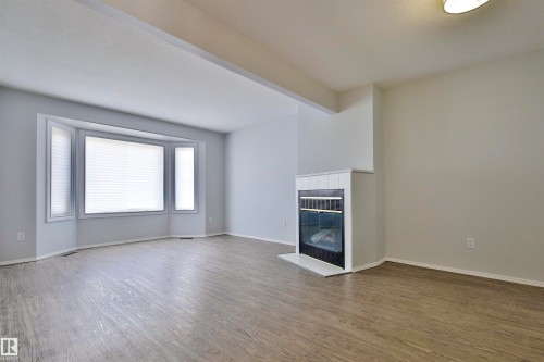 Bay window with blinds, wood-finish flooring, fireplace with a white mantel and black surround, and light wall tones - 15529 95 Avenue Nw, Edmonton, AB - Indoor With Fireplace