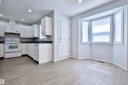 White cabinetry with dark countertops, white appliances, wood-finish flooring, and a bay window - 15529 95 Avenue Nw, Edmonton, AB - Indoor Photo Showing Kitchen