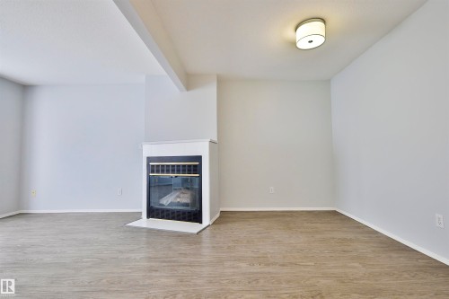 Warm interior with wood-finish flooring, a white trim fireplace with a black insert, and a flush mount ceiling light - 15529 95 Avenue Nw, Edmonton, AB - Indoor Photo Showing Other Room With Fireplace