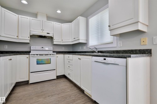White cabinetry, dark stone-finish countertops, stainless steel sink, and wood-finish flooring - 15529 95 Avenue Nw, Edmonton, AB - Indoor Photo Showing Kitchen
