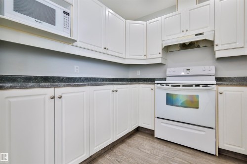 White cabinetry with brushed nickel hardware, dark countertops, built-in range, and wood-finish flooring - 15529 95 Avenue Nw, Edmonton, AB - Indoor Photo Showing Kitchen