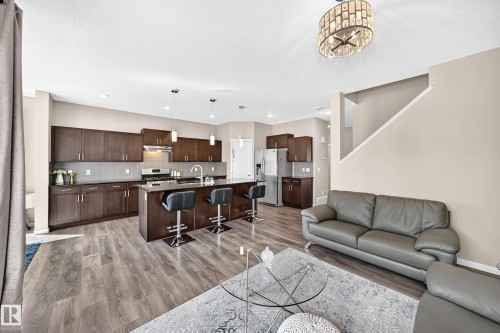 Expansive kitchen featuring dark wood cabinetry, stainless steel appliances, a large island with seating, and wood-finish flooring - 5147 Crabapple Link Sw, Edmonton, AB - Indoor