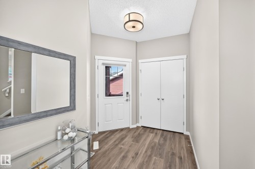 Entryway featuring wood-finish flooring, a contemporary ceiling light fixture, a white paneled door with glass insert, and double bi-fold closet doors - 5147 Crabapple Link Sw, Edmonton, AB - Indoor Photo Showing Other Room