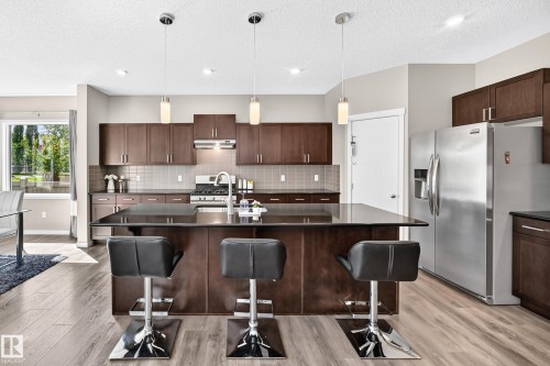 Kitchen featuring wood-finish flooring, dark wood cabinetry, stainless steel appliances, and a central island with a dark countertop - 5147 Crabapple Link Sw, Edmonton, AB - Indoor Photo Showing Kitchen With Double Sink With Upgraded Kitchen