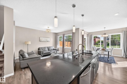Kitchen island with a stainless steel sink and faucet, pendant lighting, wood-finish flooring, and multiple windows - 5147 Crabapple Link Sw, Edmonton, AB - Indoor Photo Showing Kitchen With Double Sink With Upgraded Kitchen