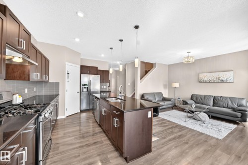 Open-concept living space featuring wood-finish flooring, a kitchen island with integrated sink, stainless steel appliances, and dark wood cabinetry - 5147 Crabapple Link Sw, Edmonton, AB - Indoor Photo Showing Kitchen With Double Sink With Upgraded Kitchen