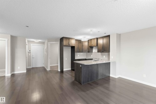 Open-concept living space featuring wood-finish flooring, a kitchen with dark cabinetry, stone countertops, and a full-size refrigerator enclosure - #114 2207 44 Av Nw, Edmonton, AB - Indoor Photo Showing Kitchen
