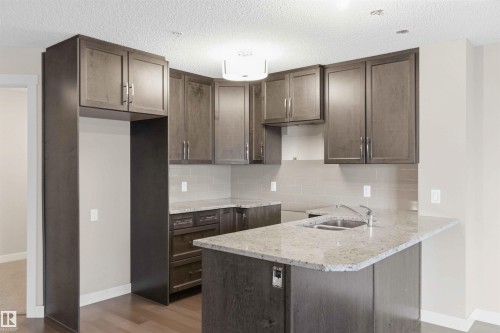 Kitchen featuring wood-finish flooring, dark wood cabinetry, light-toned countertops, a light gray subway tile backsplash, and a double basin sink with a chrome faucet - #114 2207 44 Av Nw, Edmonton, AB - Indoor Photo Showing Kitchen With Double Sink
