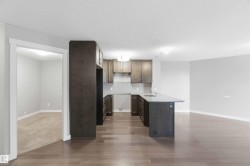 Open-concept kitchen featuring dark wood cabinetry, light-toned countertops, an island with a sink, and integrated appliances - 