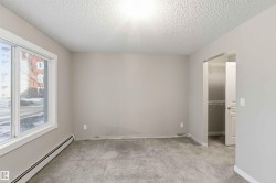 Carpeted room featuring a large window with white trim, baseboard heating, a neutral wall color, and an open doorway revealing a closet with wire shelving - 