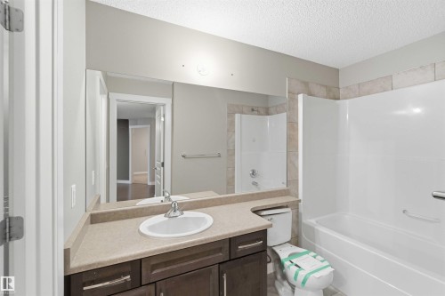 Modern bathroom featuring a single vanity with wood-finish cabinetry, a light-toned countertop, and a large mirror - #114 2207 44 Av Nw, Edmonton, AB - Indoor Photo Showing Bathroom