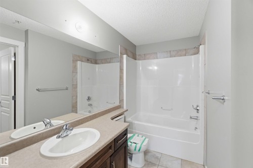 Bathroom featuring a single vanity with an oval sink and chrome faucet, a large wall-mounted mirror, a tub/shower combination with tile surround, and light-toned floor tiles - #114 2207 44 Av Nw, Edmonton, AB - Indoor Photo Showing Bathroom