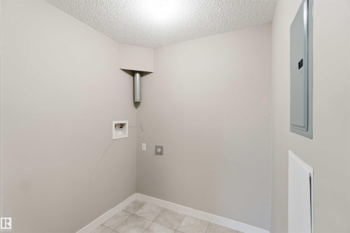 Dedicated utility space featuring light neutral wall paint, a textured ceiling, and large format square floor tiles - #114 2207 44 Av Nw, Edmonton, AB - Indoor Photo Showing Other Room