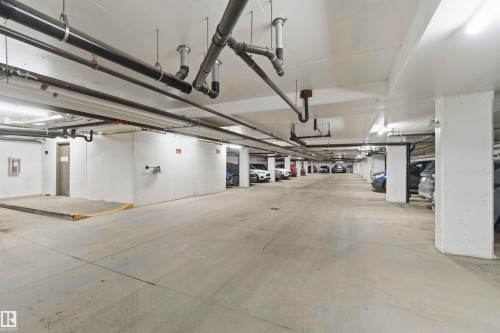 Underground parking garage featuring concrete flooring, exposed overhead piping, and fluorescent lighting - #114 2207 44 Av Nw, Edmonton, AB - Indoor Photo Showing Garage