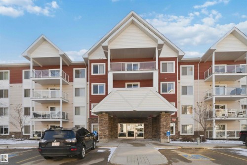 Contemporary apartment building exterior featuring a prominent covered entryway, multiple levels of private balconies with glass railings, and a striking red and white facade - #114 2207 44 Av Nw, Edmonton, AB - Outdoor With Facade