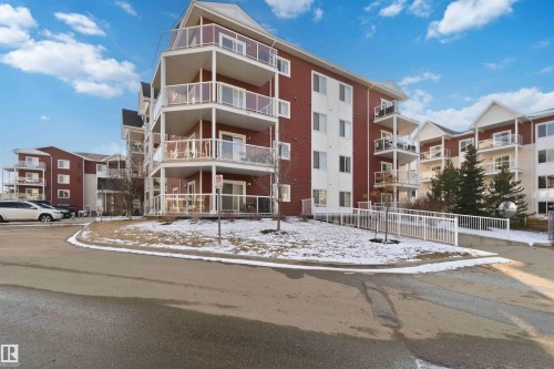Multi-story residential building featuring red and white exterior siding, multiple balconies with glass railings, and ground-level access ramps - #114 2207 44 Av Nw, Edmonton, AB - Outdoor With Facade