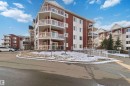 Multi-story residential building featuring red and white exterior siding, multiple balconies with glass railings, and ground-level access ramps - #114 2207 44 Av Nw, Edmonton, AB  - Outdoor With Facade 