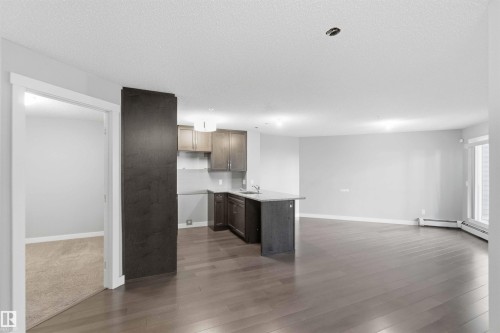 Contemporary kitchen featuring dark wood-finish cabinetry, a peninsula island with a sink, and light countertops - #114 2207 44 Av Nw, Edmonton, AB - Indoor Photo Showing Kitchen