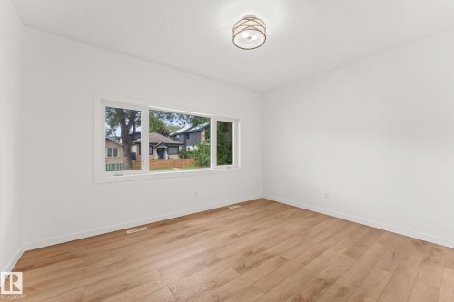 Spacious room featuring wood-finish flooring, white walls, and a modern semi-flush mount ceiling fixture - 10825 93 Street Nw, Edmonton, AB - Indoor Photo Showing Other Room