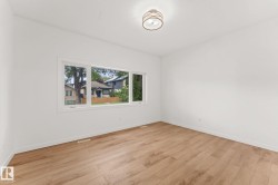 Spacious room featuring wood-finish flooring, white walls, and a modern semi-flush mount ceiling fixture - 