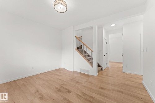 Light wood-finish flooring, staircase with carpeted treads and wood handrail, white walls, and a contemporary ceiling light fixture - 10825 93 Street Nw, Edmonton, AB - Indoor Photo Showing Other Room