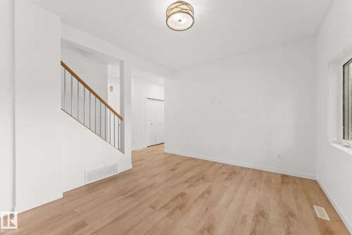 Light wood-finish flooring, white walls, flush-mount ceiling fixture, window, and a staircase with wood railing and metal balusters - 10825 93 Street Nw, Edmonton, AB - Indoor Photo Showing Other Room