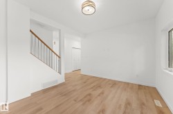Light wood-finish flooring, white walls, flush-mount ceiling fixture, window, and a staircase with wood railing and metal balusters - 