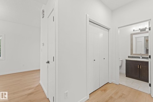 Light wood-finish flooring, white walls, white bi-fold closet doors, dark wood vanity with a white countertop, and a tiled bathroom floor - 10825 93 Street Nw, Edmonton, AB - Indoor Photo Showing Other Room