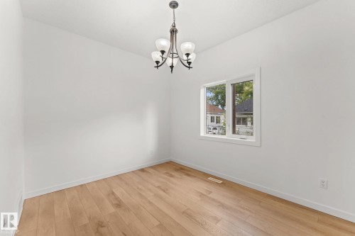 Light wood-finish flooring, white walls, and a multi-arm chandelier with frosted glass shades - 10825 93 Street Nw, Edmonton, AB - Indoor Photo Showing Other Room