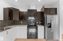 Kitchen featuring two-tone cabinetry, a tile backsplash, stainless steel sink, and stainless steel refrigerator - 