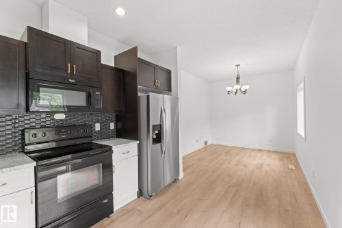 Kitchen featuring dark wood-finish cabinetry, stainless steel appliances, mosaic tile backsplash, and light wood-finish flooring - 10825 93 Street Nw, Edmonton, AB - Indoor Photo Showing Kitchen