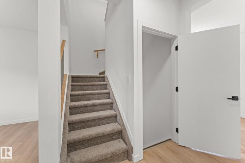 Hardwood-style flooring, carpeted staircase, light wood handrail, and white panel door with black hardware - 10825 93 Street Nw, Edmonton, AB - Indoor Photo Showing Other Room